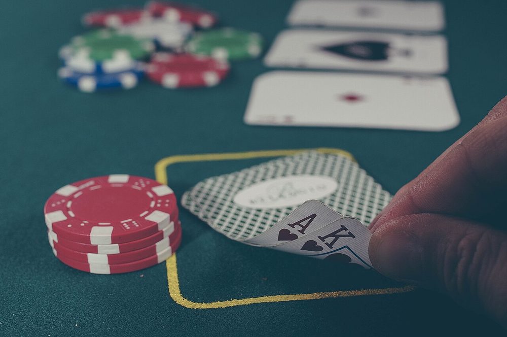 A hand holding playing cards over a green card table